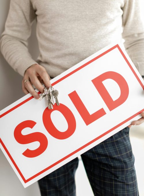 Close-up of a realtor holding a sold sign and keys, symbolizing successful property sale.